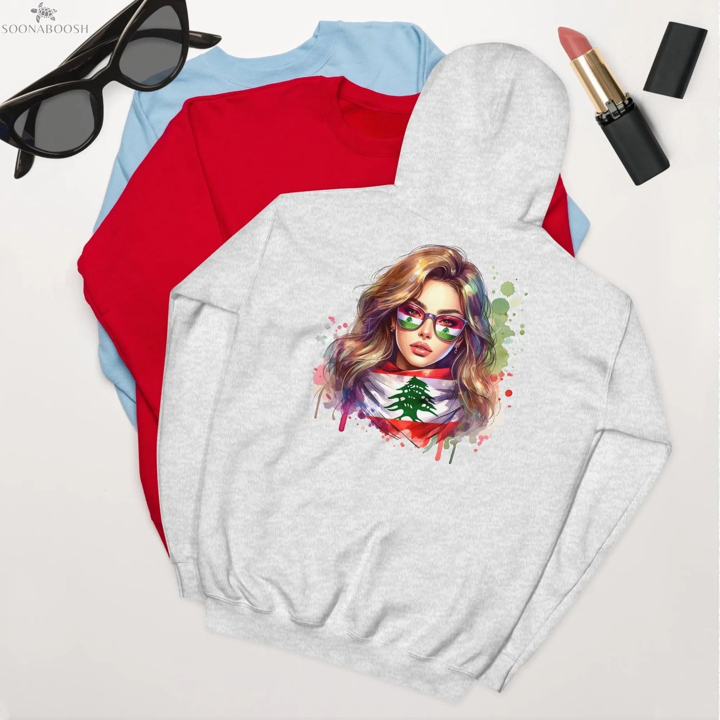A flat-lay of the 'Lebanon Pride' hoodie from Soonaboosh, showing the artistic design on the back of a woman wearing a Lebanese flag scarf, styled with sunglasses and lipstick.